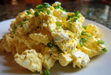 Close-up of a mound of creamy egg salad recipe garnished generously with chopped green onions on a white plate.