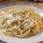 Close-up of fettuccine pasta generously coated in creamy homemade alfredo sauce and topped with black pepper.