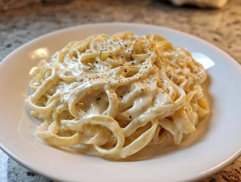 Close-up of fettuccine pasta generously coated in creamy homemade alfredo sauce and topped with black pepper.