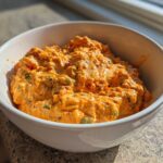 A close-up of creamy, orange Rotel dip with visible chunks of peppers served hot in a white bowl.