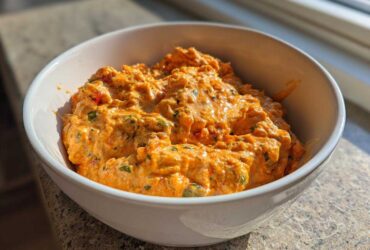 A close-up of creamy, orange Rotel dip with visible chunks of peppers served hot in a white bowl.