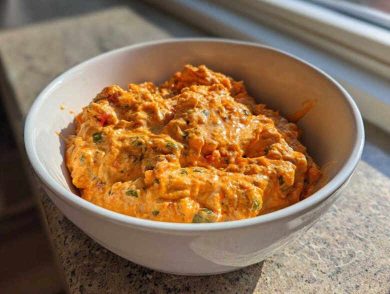 A close-up of creamy, orange Rotel dip with visible chunks of peppers served hot in a white bowl.
