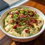 A close-up of creamy Million Dollar Dip topped generously with crumbled bacon and fresh green onions.