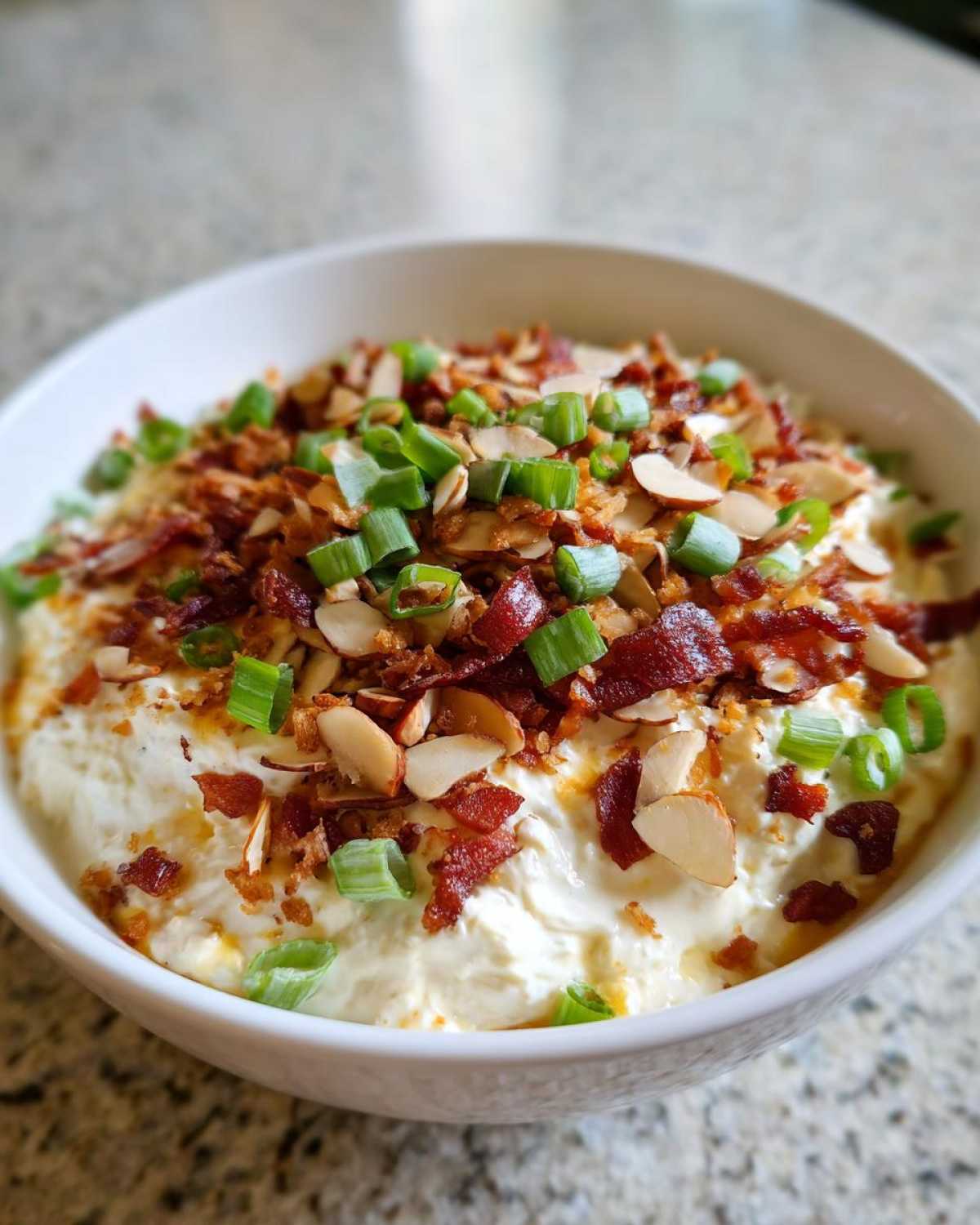 Close-up of creamy Neiman Marcus dip topped generously with crumbled bacon, sliced almonds, and chopped green onions.