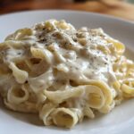 Close-up of fettuccine pasta generously coated in creamy olive garden alfredo sauce and topped with black pepper.