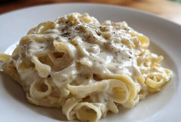 Close-up of fettuccine pasta generously coated in creamy olive garden alfredo sauce and topped with black pepper.