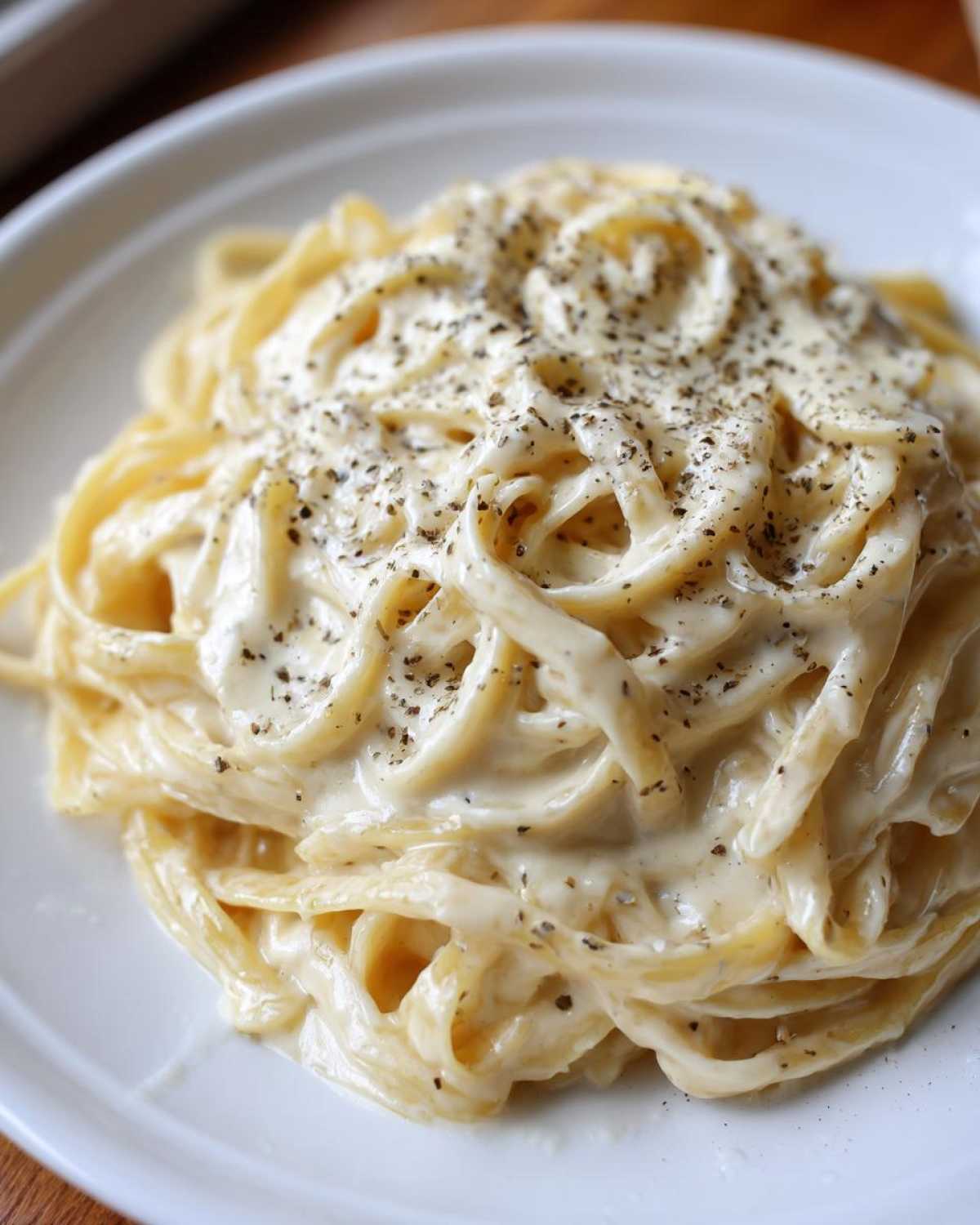 Close-up of fettuccine pasta generously coated in creamy olive garden alfredo sauce and topped with cracked black pepper.