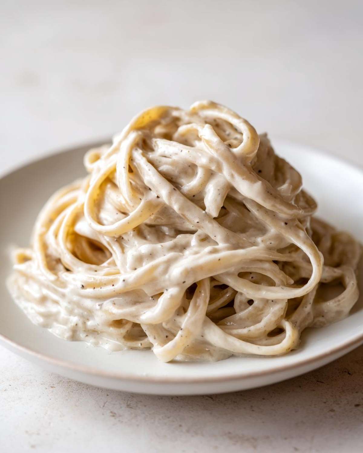 Close-up of fettuccine pasta generously coated in rich, creamy homemade alfredo sauce with visible black pepper specks.