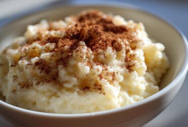 Close-up of creamy rice pudding served in a white bowl, generously topped with ground cinnamon.