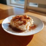 A serving of creamy rice pudding recipe generously dusted with cinnamon powder on a white plate.