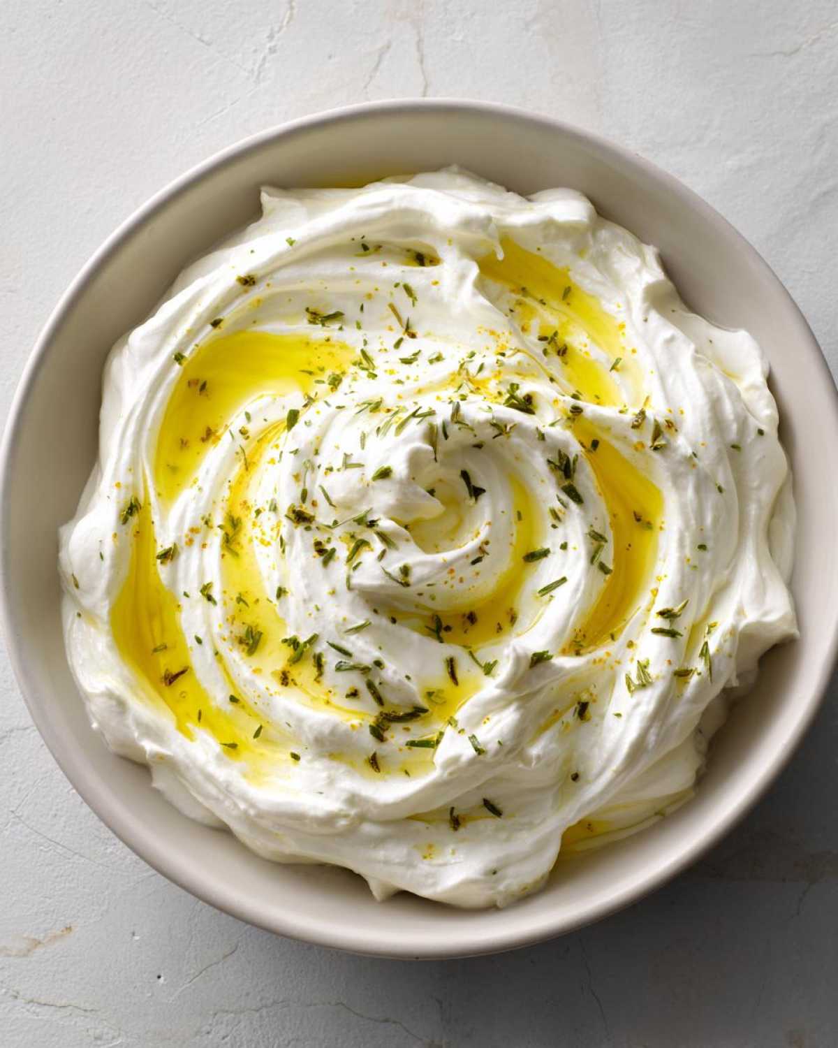 Overhead view of a bowl filled with creamy whipped feta dip, drizzled with olive oil and sprinkled with herbs.