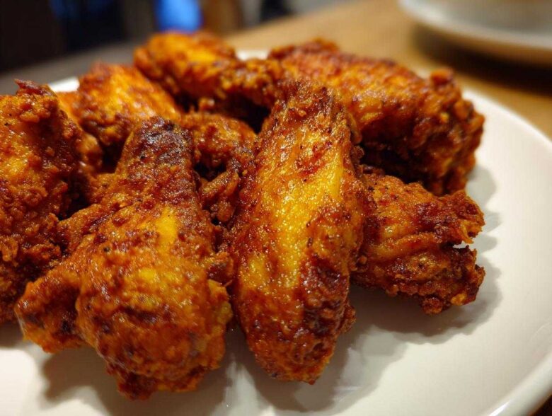 A close-up shot of several golden-brown, seasoned crispy air fryer chicken wings piled on a white plate.