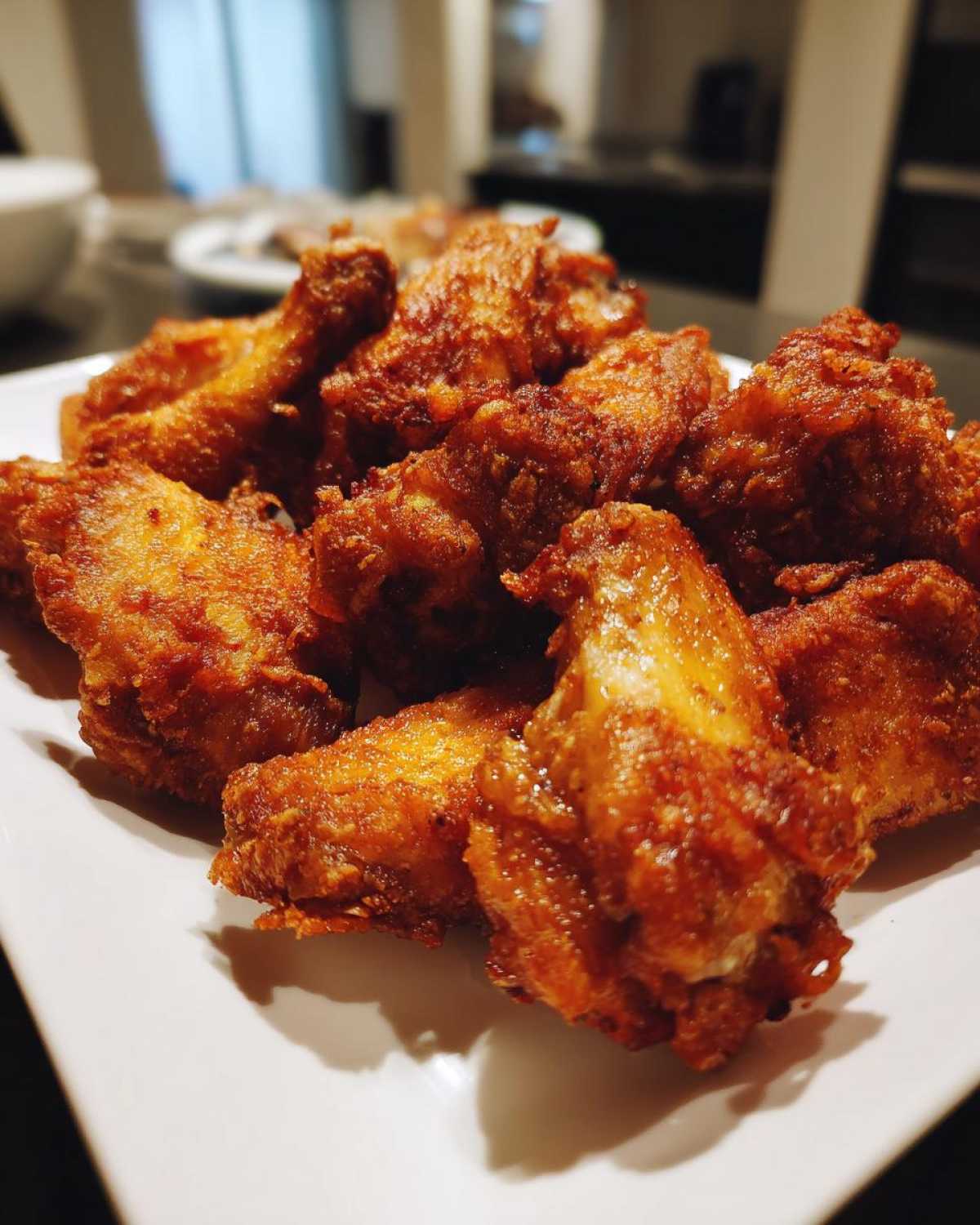 A close-up of a pile of golden brown, crispy air fryer chicken wings served on a white plate.