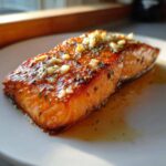 A perfectly cooked, glistening fillet of air fryer salmon topped with minced garlic and herbs, resting in its juices.