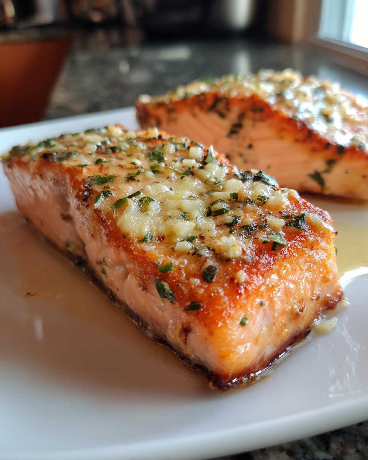 Close-up of two perfectly cooked air fryer salmon fillets topped with minced garlic and parsley.