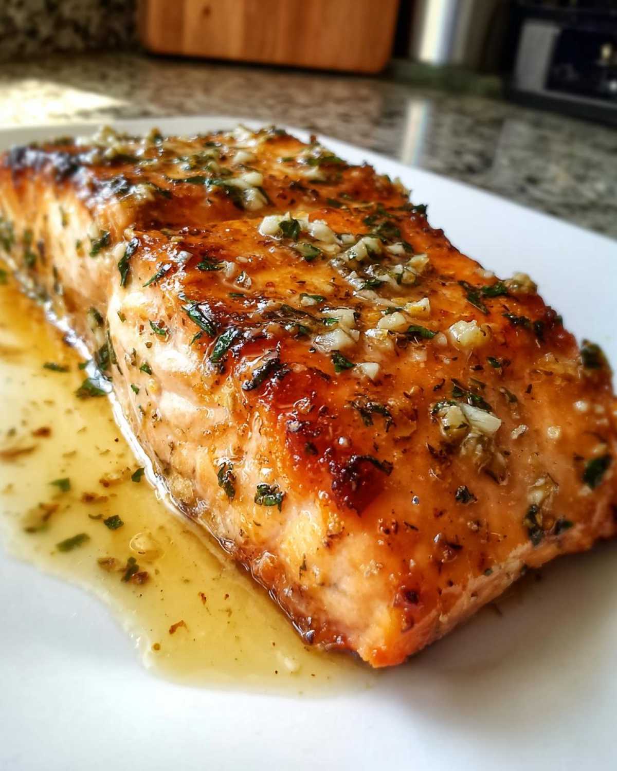 Close-up of a perfectly cooked, glazed air fryer salmon fillet topped with minced garlic and herbs.