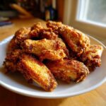A pile of golden brown, crispy baked chicken wings seasoned and served on a white plate.