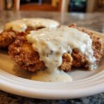 Two pieces of crispy, golden-brown chicken fried steak generously covered in creamy white pepper gravy.