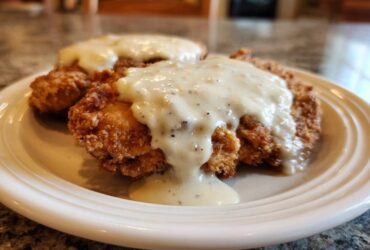 Two pieces of crispy, golden-brown chicken fried steak generously covered in creamy white pepper gravy.