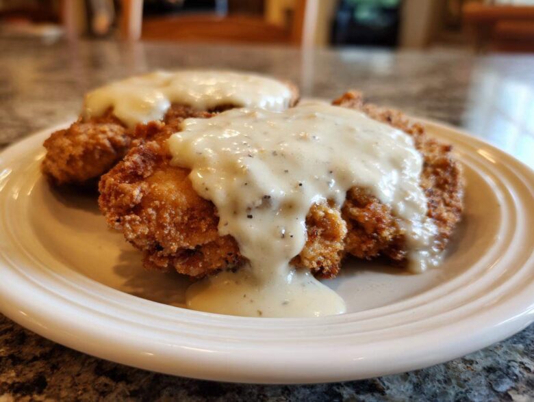 Two pieces of crispy, golden-brown chicken fried steak generously covered in creamy white pepper gravy.