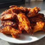 A white plate piled high with perfectly cooked, crispy, and glazed chicken wings under natural light.