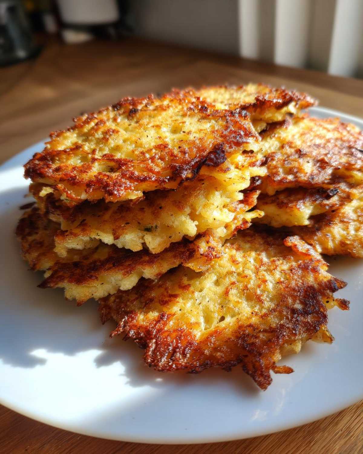 A stack of golden brown, crispy potato pancakes glistening under sunlight on a white plate.