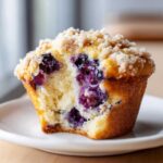 A close-up, cross-section view of a moist blueberry muffin with a sugary crumb topping, showing juicy blueberries inside.