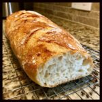 A freshly baked loaf of french bread, sliced open to show the airy interior, resting on a wire cooling rack.