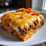 A close-up slice of Dorito Casserole topped with melted cheddar and Monterey Jack cheese and crushed chips.