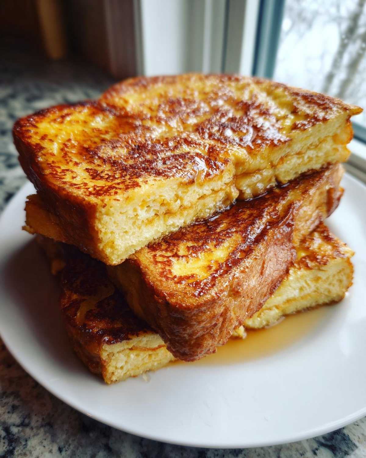 A stack of thick, golden brown easy french toast slices drizzled with syrup on a white plate.