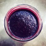 Overhead close-up view of thick, dark purple homemade elderberry syrup recipe stored in a glass jar.