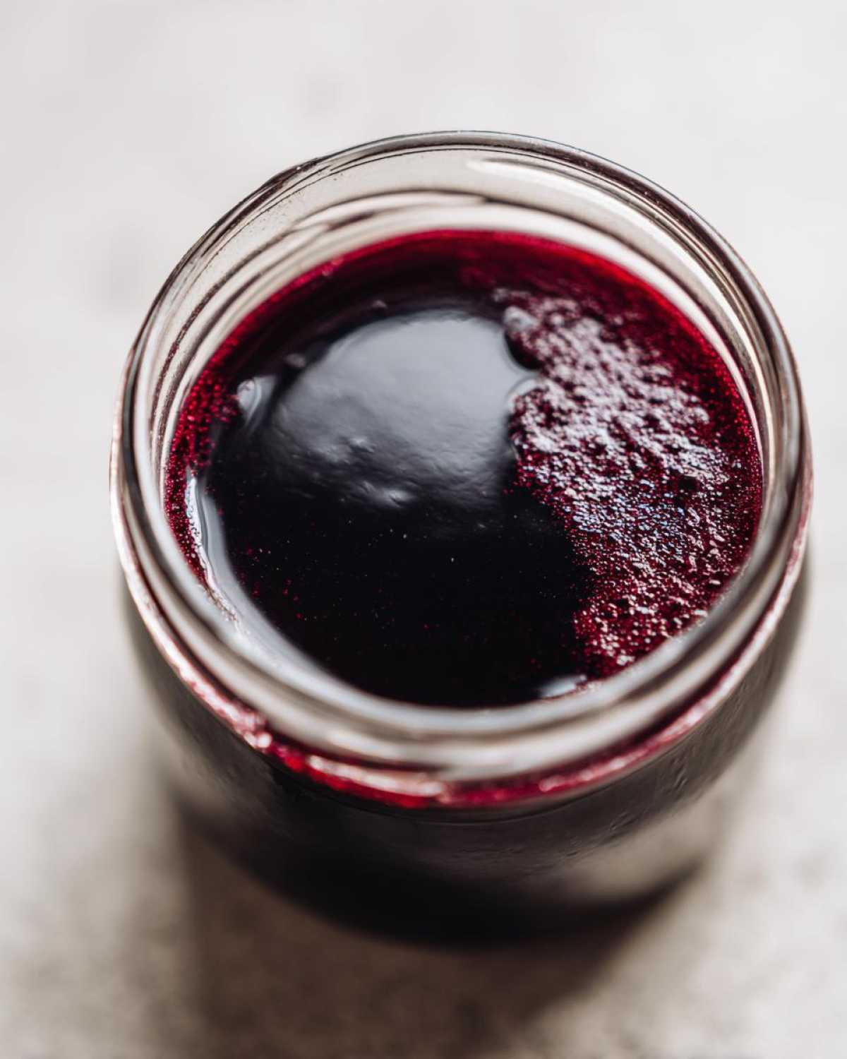 Overhead close-up view of dark, rich elderberry syrup recipe inside a glass jar, showing a slight foam layer.