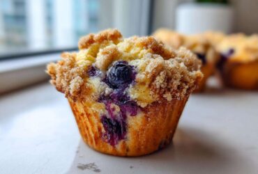 A close-up, featured image of a golden brown blueberry muffin topped with a generous layer of sugary streusel topping.