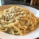Close-up of fettuccine pasta coated in creamy olive garden alfredo sauce, topped with grated cheese and black pepper.