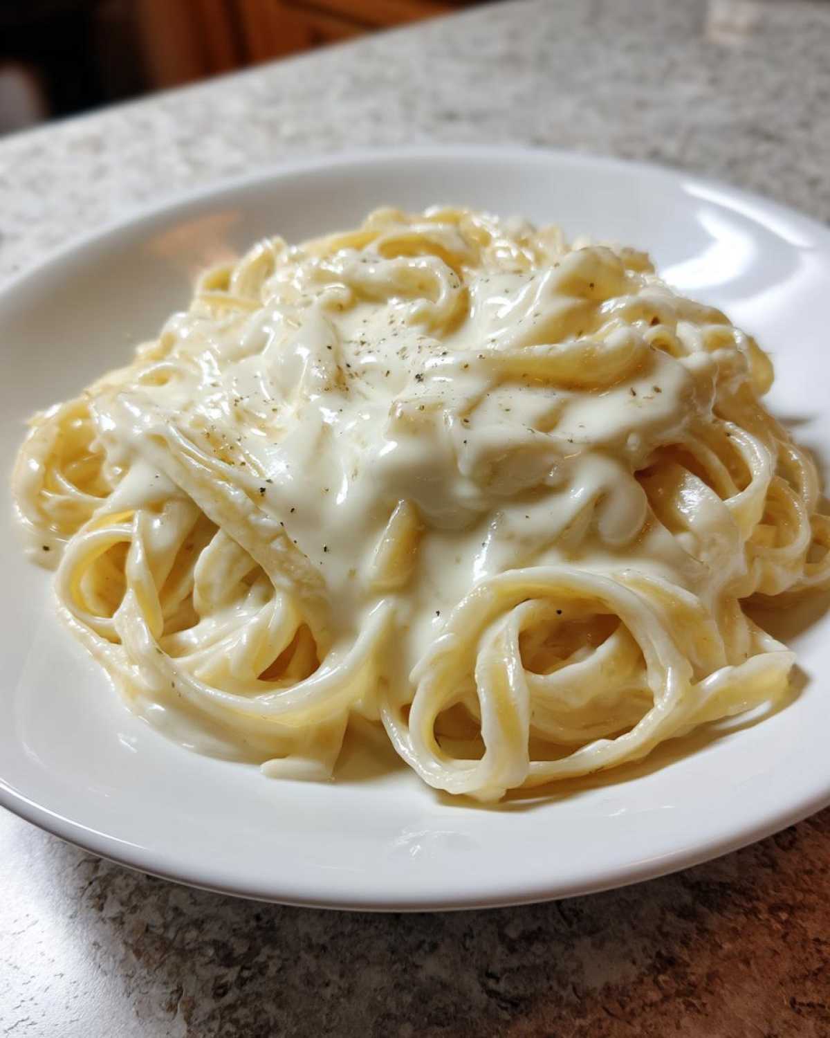A close-up of fettuccine pasta generously coated in rich homemade alfredo sauce and sprinkled with black pepper.