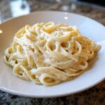Close-up of fettuccine pasta generously coated in rich, creamy homemade alfredo sauce.