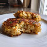 Close-up of two golden-brown maryland crab cakes on a white plate, showing the flaky crab meat inside one that is broken open.