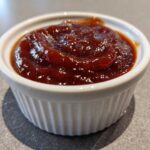 Close-up of thick, glossy, dark red homemade bbq sauce served in a small white fluted ramekin.