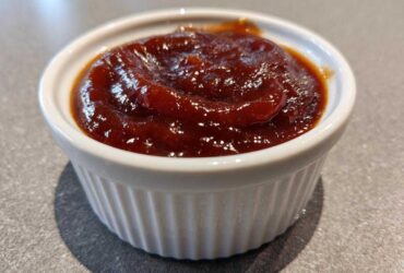 Close-up of thick, glossy, dark red homemade bbq sauce served in a small white fluted ramekin.