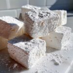 Close-up of fluffy homemade marshmallows stacked and heavily dusted with white powdered sugar.