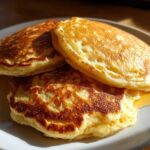 A stack of three golden brown, fluffy oatmeal pancakes drizzled with syrup on a light gray plate.