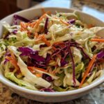 Close-up of a vibrant cabbage salad featuring shredded green and red cabbage and carrots, lightly dressed.
