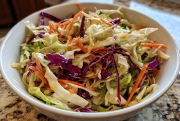 Close-up of a vibrant cabbage salad featuring shredded green and red cabbage and carrots, lightly dressed.