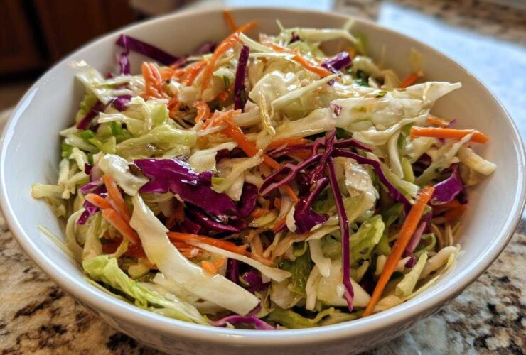 Close-up of a vibrant cabbage salad featuring shredded green and red cabbage and carrots, lightly dressed.