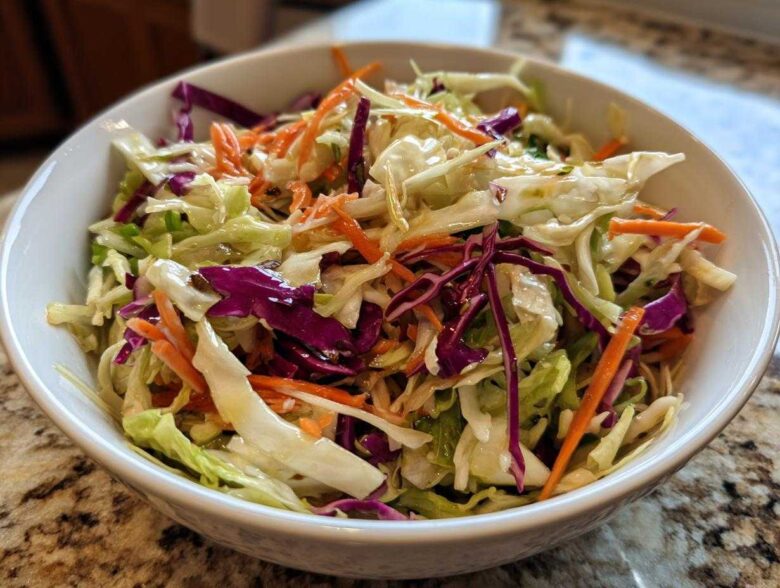Close-up of a vibrant cabbage salad featuring shredded green and red cabbage and carrots, lightly dressed.