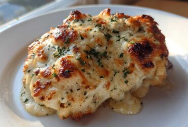 A close-up of a serving of Garlic parmesan chicken bake covered in melted, golden-brown cheese and parsley.