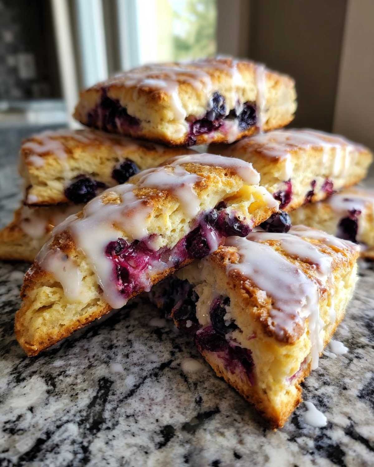 Close-up of a stack of moist blueberry scones drizzled with white glaze, showing juicy blueberries inside.