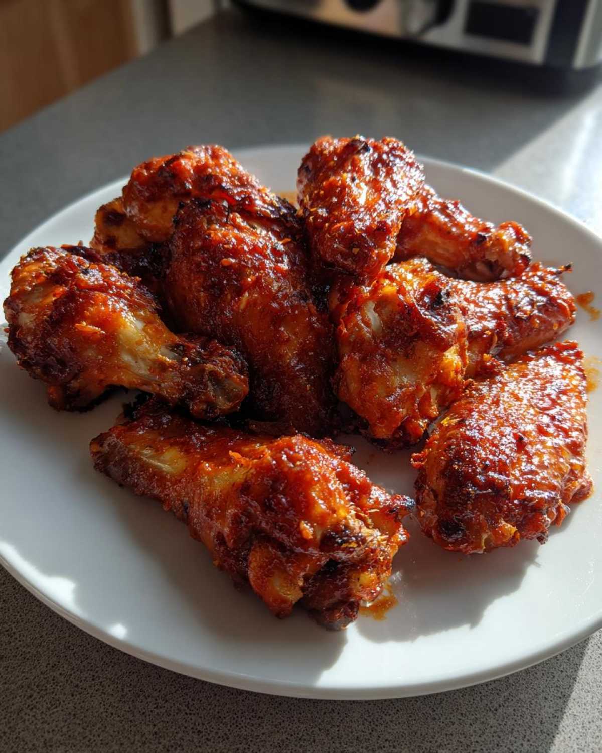 Close-up of several saucy, glazed chicken wings piled on a white plate, glistening in natural sunlight.