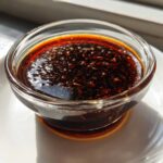Close-up of thick, dark homemade teriyaki sauce with visible specks of seasoning in a small glass bowl.