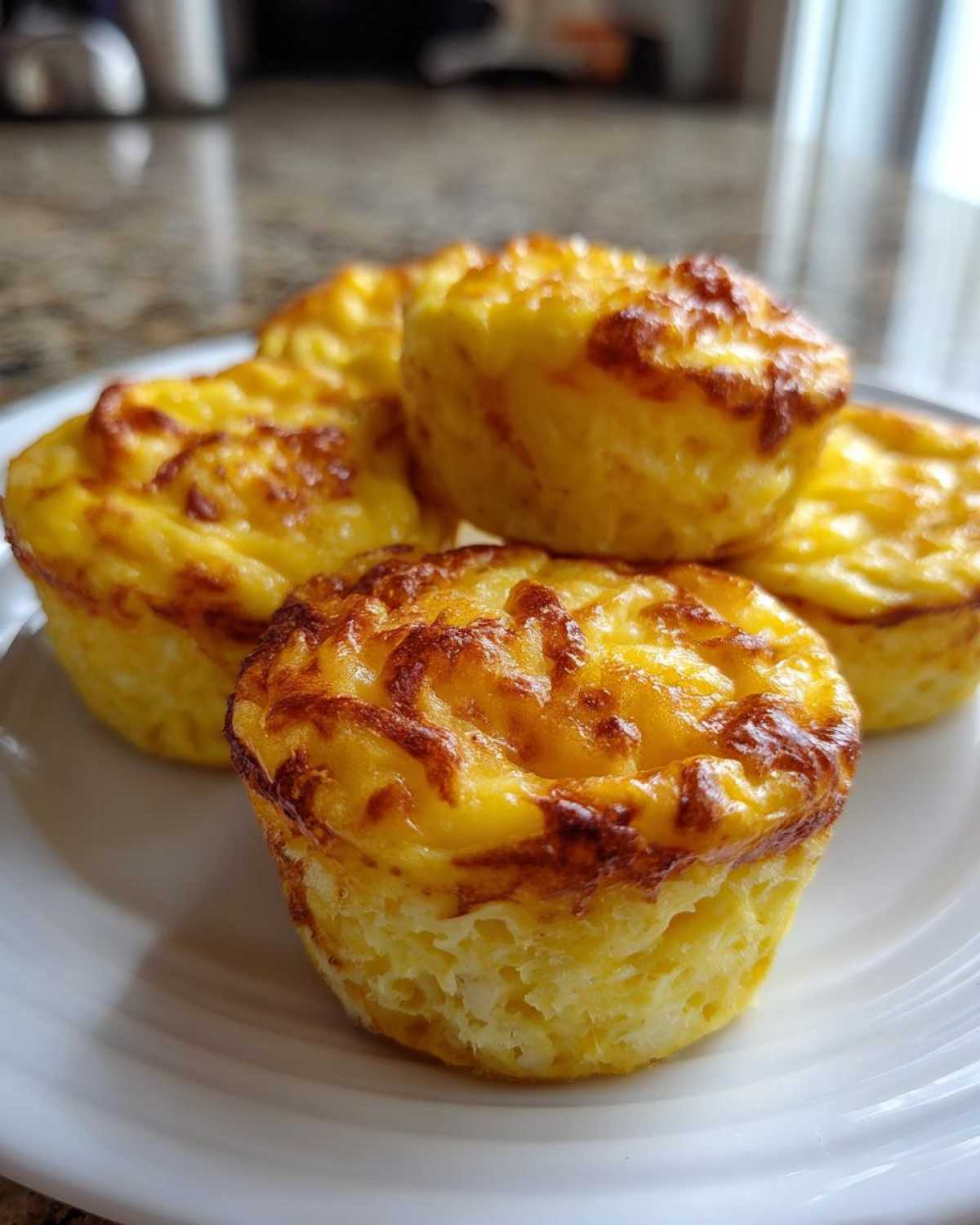 A close-up of several fluffy, golden brown baked egg bites stacked on a white plate.